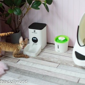 May include: A white automatic pet feeder with a digital timer, a white water fountain with a green top and a white pet bed with a black rim.