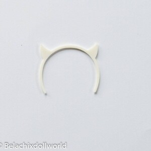 May include: White plastic devil horn headband. The headband is a simple circle with two small horns on the top.
