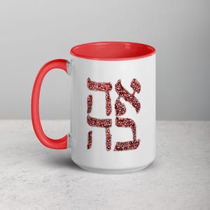 May include: White ceramic mug with a red interior and handle. The mug features Hebrew text in a red floral pattern. The mug is designed for hot or cold beverages.