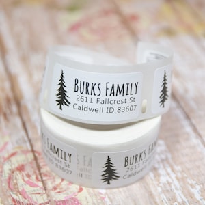 May include: Roll of white address labels with a black silhouette of a pine tree and the text "BURKS FAMILY 2611 Fallcrest St Caldwell ID 83607".