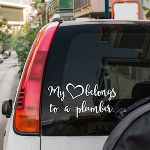 May include: A white car with a sticker on the back window that says "My heart belongs to a plumber."