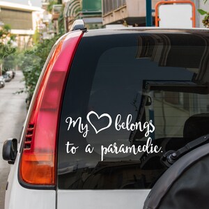 May include: White vinyl decal with the text "My heart belongs to a paramedic." on a black car window.