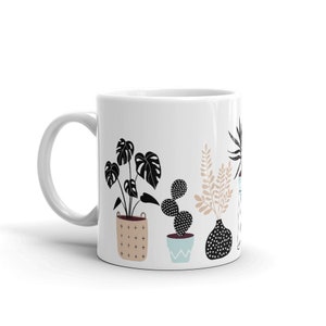 May include: White ceramic mug with a black and white illustration of potted plants. The plants include a cactus, a monstera, and a fern. The pots are decorated with black and white patterns.