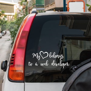 May include: A white car with a sticker on the back window that says "My heart belongs to a web developer." The sticker features a heart with a swirl design.
