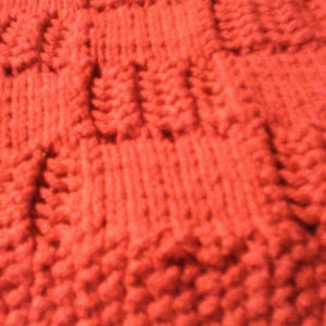 May include: Close-up of a red knitted fabric with a textured pattern. The fabric is soft and fluffy, and the pattern is created by the way the yarn is woven together.