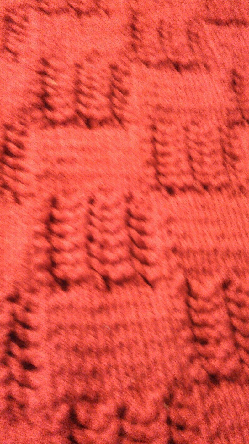 May include: A close-up of a red textured fabric with a blurred pattern of repeating shapes.