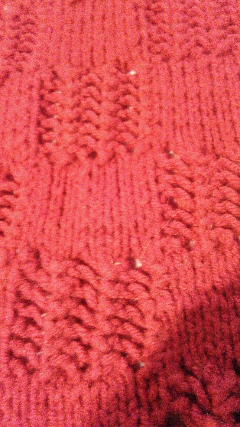 May include: Close-up of a red knitted fabric with a textured pattern. The fabric is soft and fluffy, and the texture is created by the way the yarn is woven together.