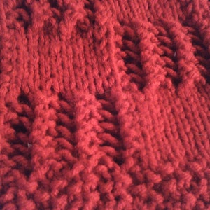 May include: Close-up of a red knitted fabric with a textured pattern. The fabric is soft and fluffy, and the texture is created by the way the yarn is woven together.