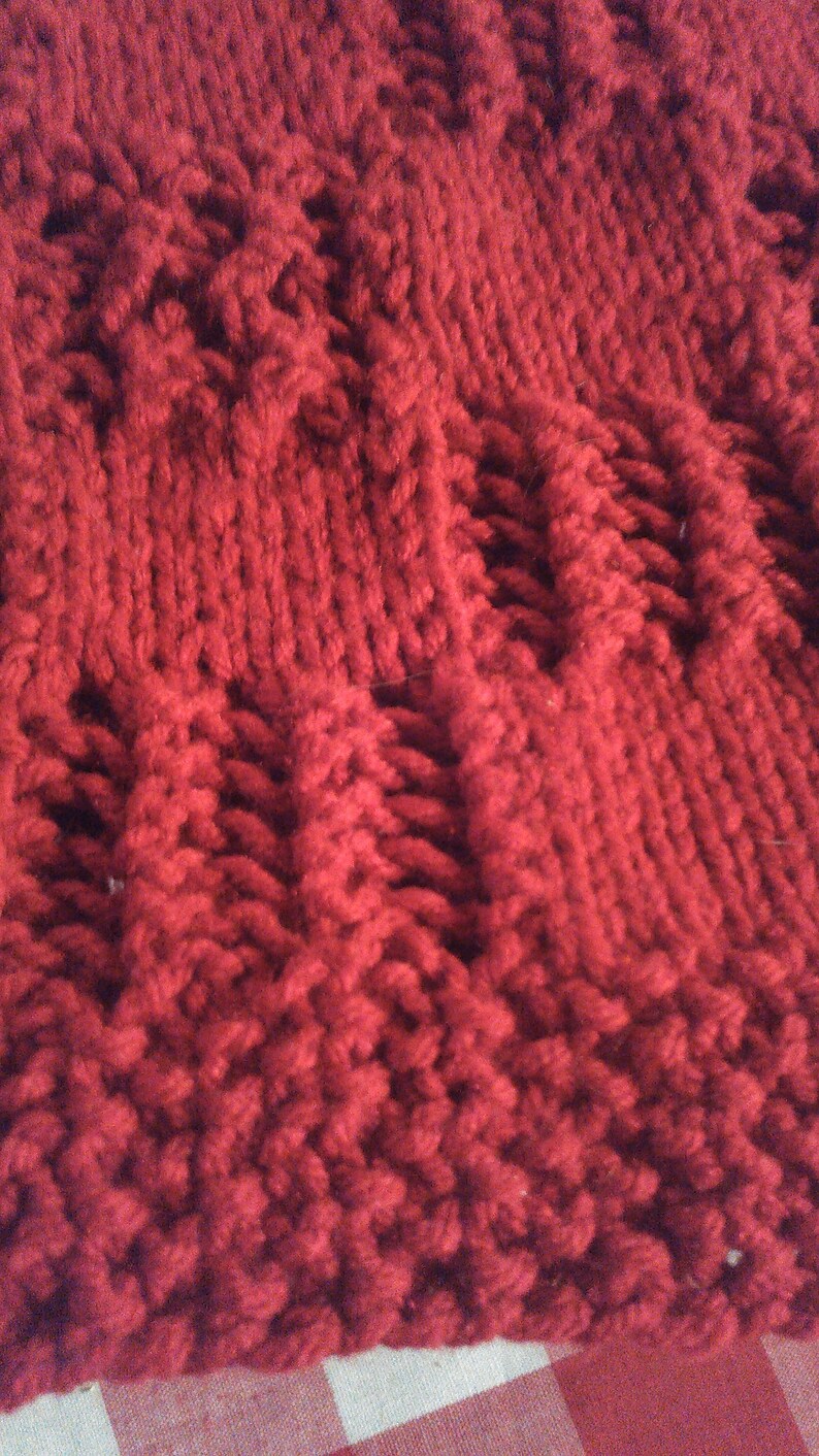 May include: Close-up of a red knitted fabric with a textured pattern. The fabric is soft and fluffy, and the texture is created by the way the yarn is woven together.