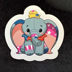 Puede incluir: Un elefante de dibujos animados, gris, de estilo patchwork, con orejas rosas, un sombrero amarillo y una pajarita roja. El elefante está sentado con las piernas cruzadas.