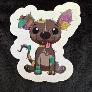 May include: A sticker featuring a cartoon dog with patchwork details. The dog has brown fur, a pink tongue, and multi-colored patches on its ears, tail, and legs. The design includes stitched lines and a playful expression.