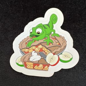 May include: A green chameleon cartoon character with a long tongue is perched on top of a brown pie crust filled with red apple slices. The pie is surrounded by green apple slices.