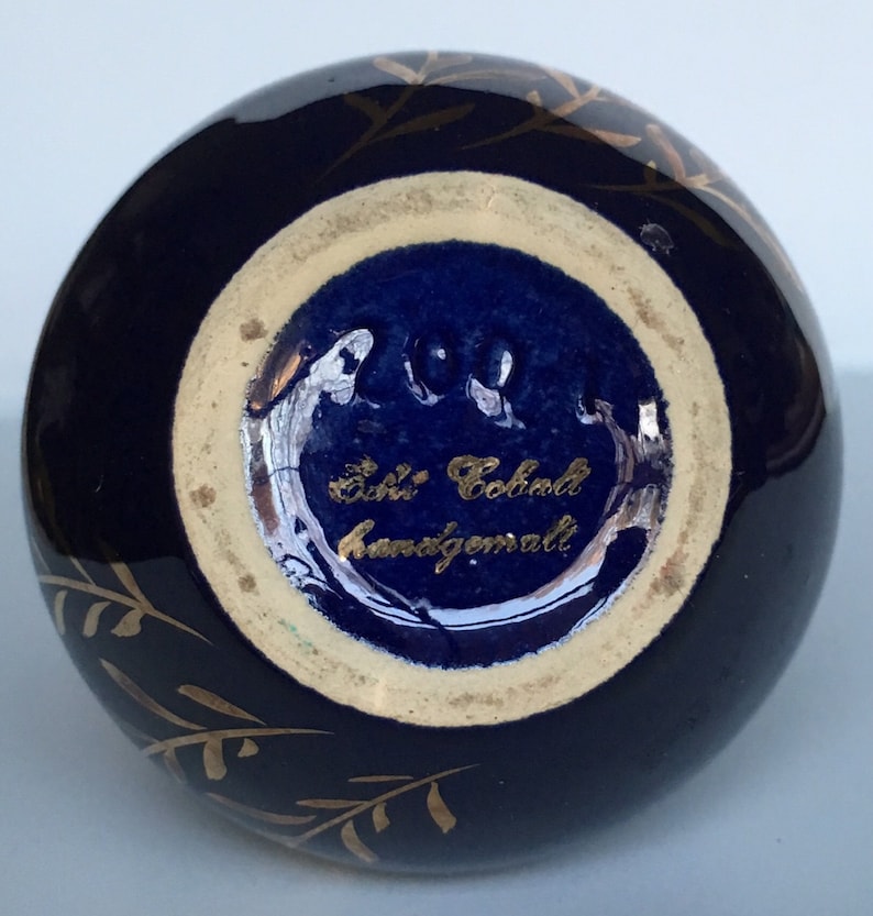 May include: A cobalt blue ceramic vase with gold leaf detailing and a gold inscription that reads "Echt Kobalt handgemalt".