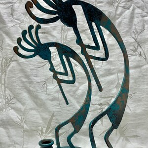 May include: A teal blue metal sculpture of two Kokopelli figures, a traditional Native American flute player, with a small teal blue pot for a candle holder.