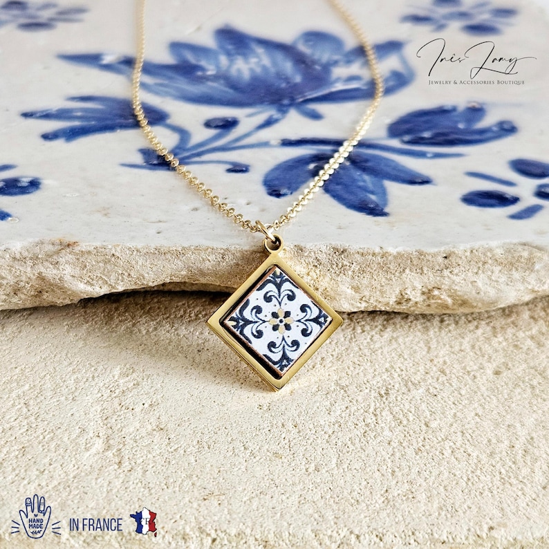 May include: Gold chain necklace with a square pendant featuring a white and blue patterned tile design.