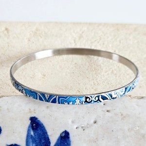 May include: A silver bangle bracelet with a blue and white patterned design.