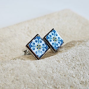 May include: A pair of silver cufflinks with a blue and white tile pattern. The tile pattern features a yellow flower in the center.