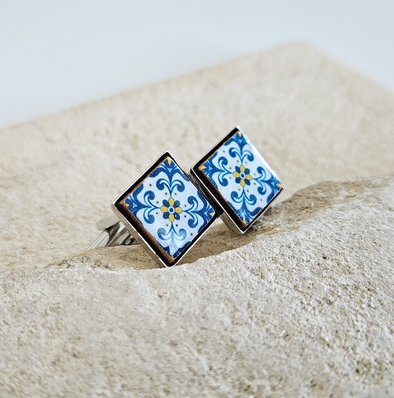 May include: A pair of silver cufflinks with a blue and white tile pattern. The tile pattern features a yellow flower in the center.