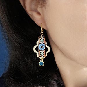 Peut inclure: Boucles d'oreilles pendantes dor&eacute;es avec un pendentif rectangulaire &agrave; motifs bleus et orange et une goutte de cristal bleu.