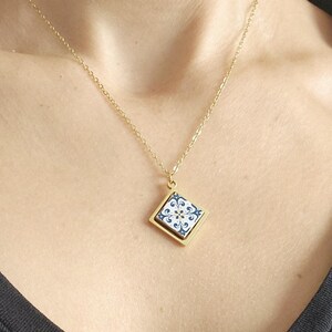 May include: A gold chain necklace with a square pendant featuring a blue and white patterned tile design.