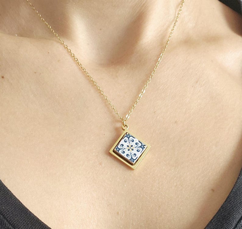 May include: A gold chain necklace with a square pendant featuring a blue and white patterned tile design.