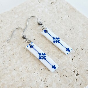 May include: A pair of silver dangle earrings with white ceramic rectangular charms. The charms have a blue and white floral pattern.