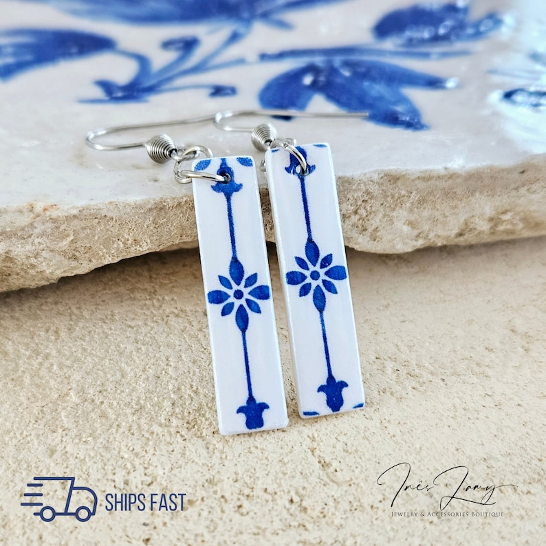 May include: A pair of blue and white ceramic tile earrings with silver hooks. The tiles feature a repeating floral pattern.