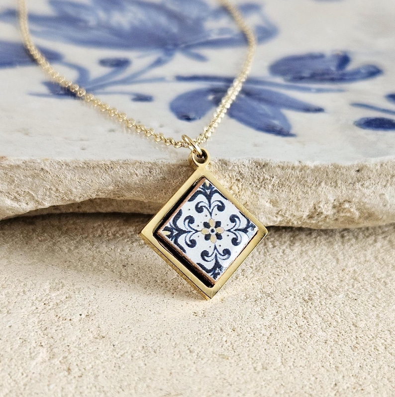 May include: A gold necklace with a square pendant featuring a white and blue patterned tile design.