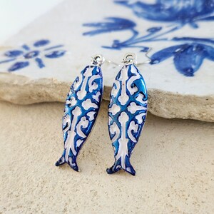 May include: A pair of blue and white fish-shaped earrings with a silver hook. The fish have a white and blue patterned design.
