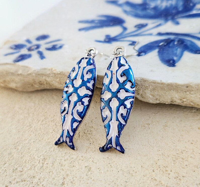 May include: A pair of blue and white fish-shaped earrings with a silver hook. The fish have a white and blue patterned design.