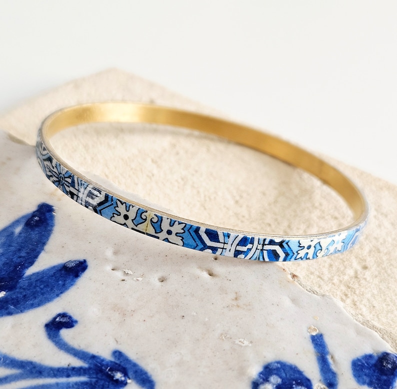 May include: A gold bangle bracelet with a blue and white patterned design. The pattern is reminiscent of traditional Portuguese tiles.