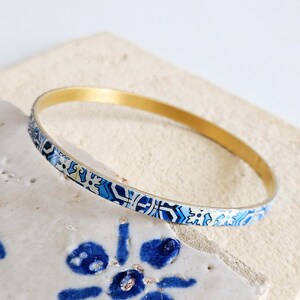 May include: A gold bangle bracelet with a blue and white patterned design. The pattern is reminiscent of traditional Portuguese tiles.