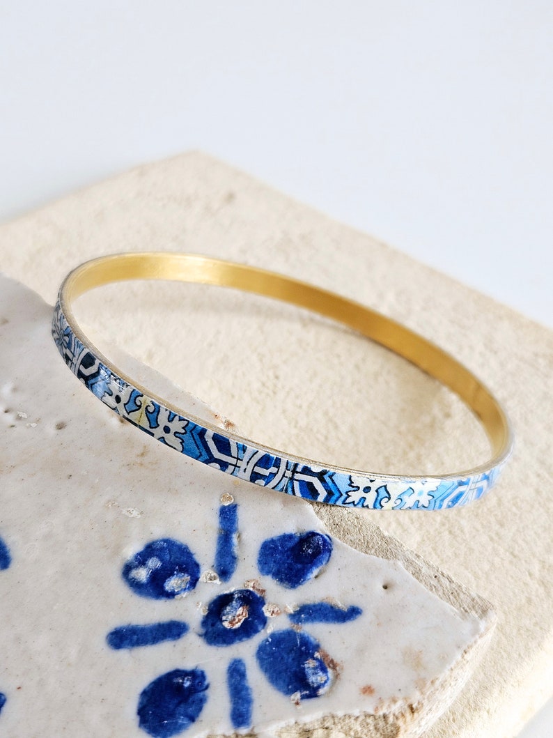 May include: A gold bangle bracelet with a blue and white patterned design. The pattern is reminiscent of traditional Portuguese tiles.