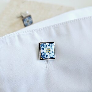 May include: A pair of cufflinks with a blue and white tile pattern. The cufflinks are silver and have a square shape.