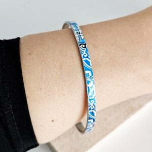 May include: A silver bangle bracelet with a blue and white patterned design.