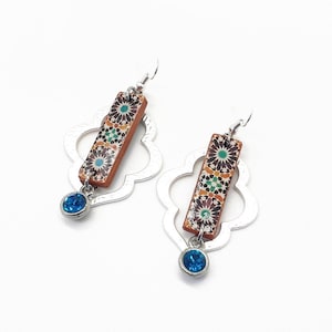 Peut inclure: Une paire de boucles d'oreilles en argent avec un motif g&eacute;om&eacute;trique. Chaque boucle d'oreille pr&eacute;sente une tuile rectangulaire avec un motif floral color&eacute; et un pendentif en cristal bleu.