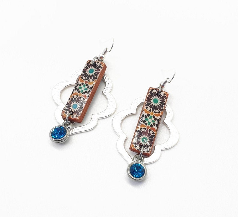Peut inclure: Une paire de boucles d'oreilles en argent avec un motif g&eacute;om&eacute;trique. Chaque boucle d'oreille pr&eacute;sente une tuile rectangulaire avec un motif floral color&eacute; et un pendentif en cristal bleu.