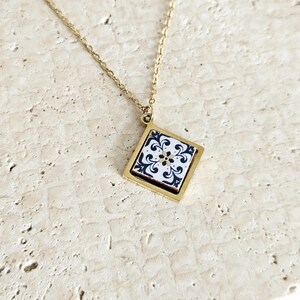 May include: Gold chain necklace with a square pendant featuring a black and white tile design.