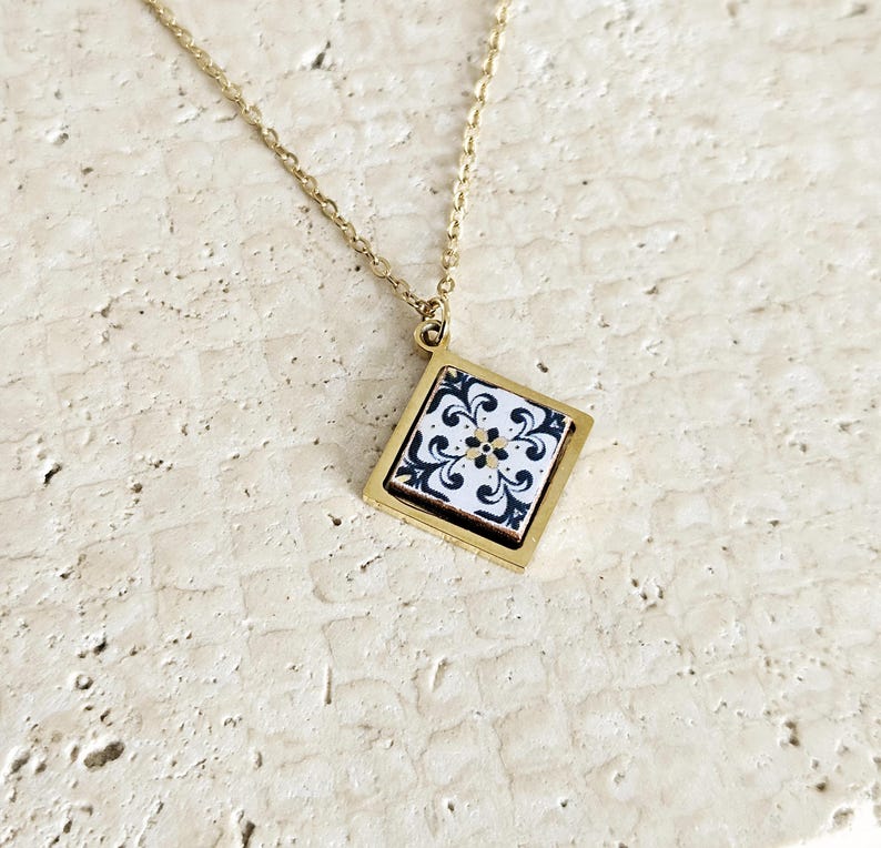 May include: Gold chain necklace with a square pendant featuring a black and white tile design.
