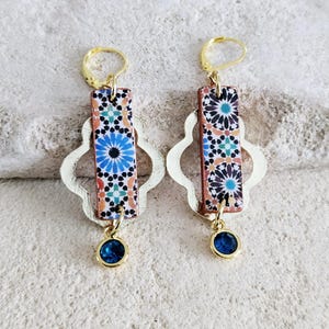 Peut inclure: Une paire de boucles d'oreilles en or avec un motif de carrelage bleu et blanc et une pierre pr&eacute;cieuse bleue suspendue. Les boucles d'oreilles ont un anneau en or et un motif de tr&egrave;fle &agrave; quatre feuilles en or.