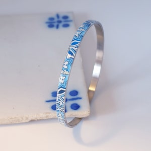 May include: A silver bangle bracelet with a blue and white patterned design.