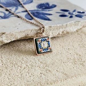 Peut inclure: Collier en chaîne dorée avec un pendentif carré orné d'un motif de carrelage bleu, vert, blanc et orange avec la lettre "F" au centre.