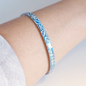 May include: A blue and white patterned bangle bracelet. The bracelet is made of metal and has a shiny finish.
