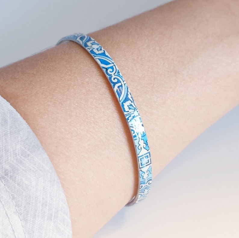 May include: A blue and white patterned bangle bracelet. The bracelet is made of metal and has a shiny finish.