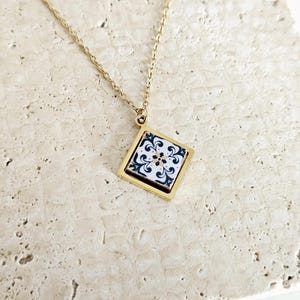 May include: A gold chain necklace with a square pendant featuring a white and black patterned tile design.