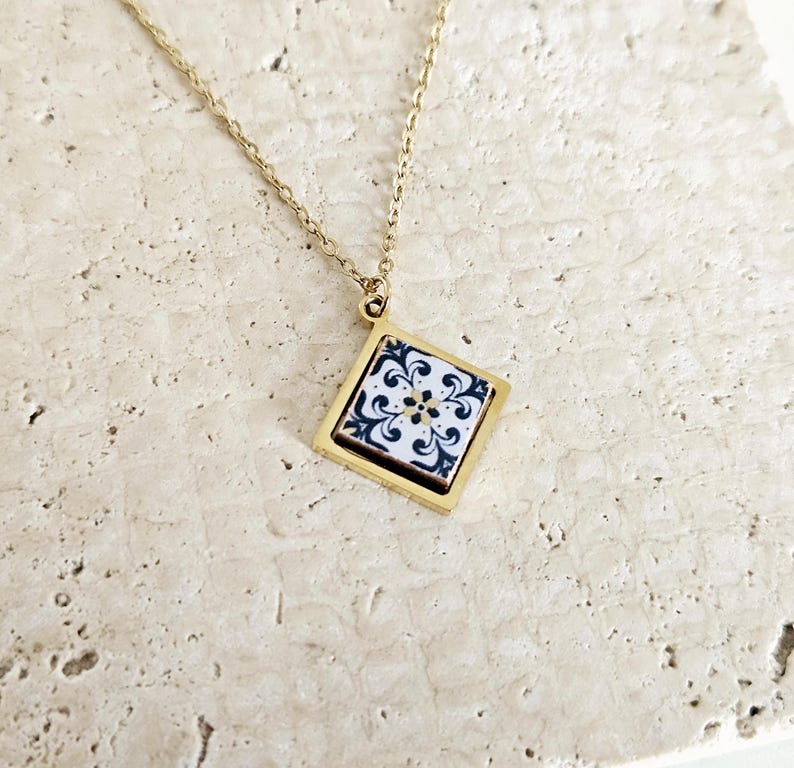 May include: A gold chain necklace with a square pendant featuring a white and black patterned tile design.