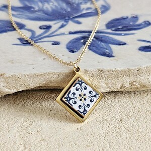May include: A gold chain necklace with a square pendant featuring a white and blue patterned tile design.