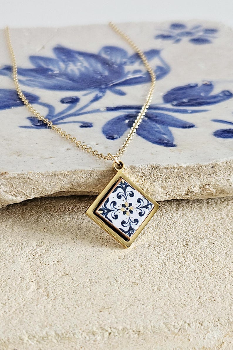 May include: A gold chain necklace with a square pendant featuring a white and blue patterned tile design.
