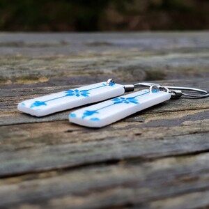 May include: A pair of white ceramic earrings with a blue floral pattern and silver hooks.