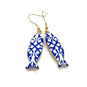 May include: A pair of blue and white fish-shaped earrings with a gold hook. The fish have a white background with a blue floral pattern.